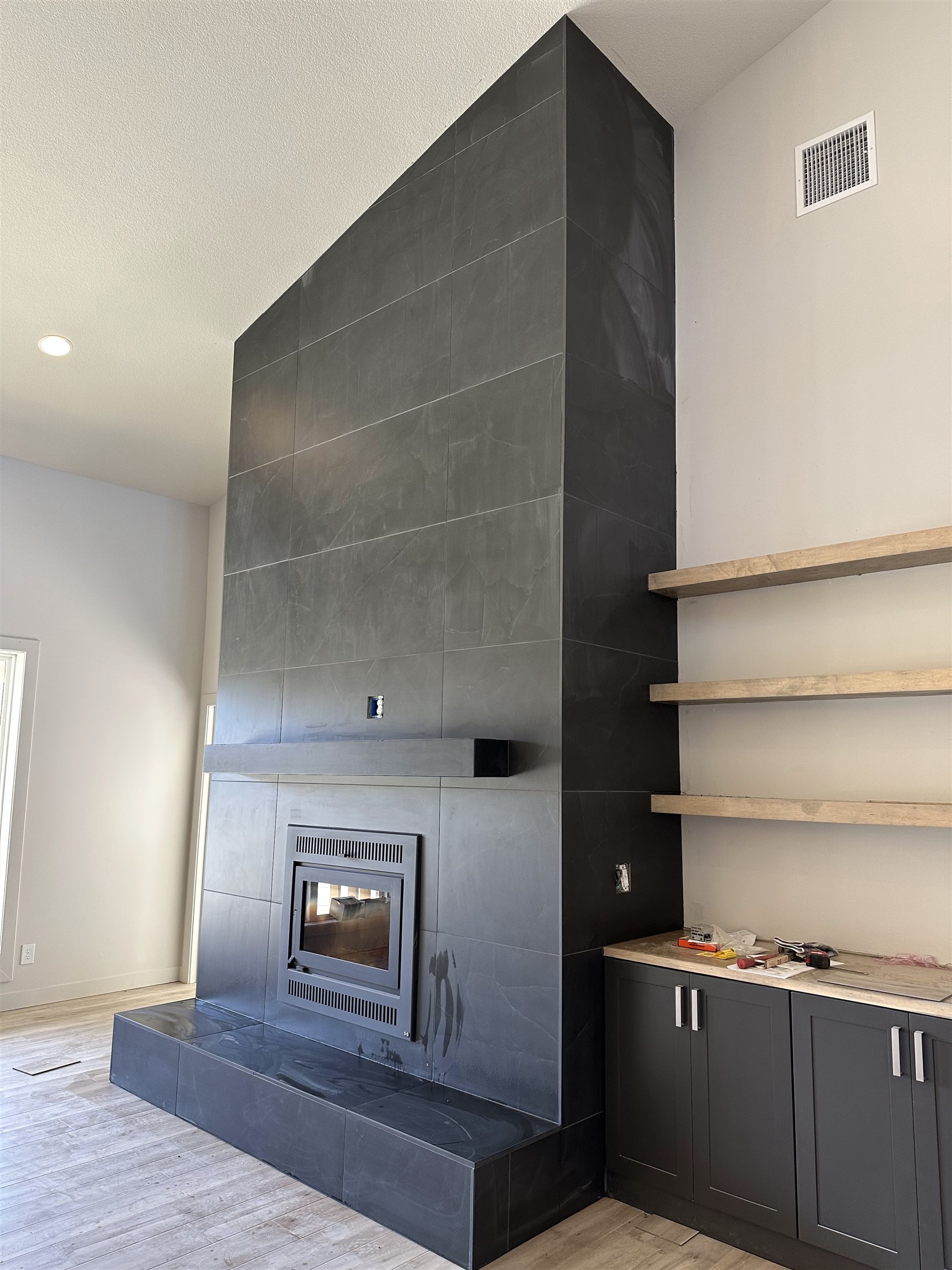 Heartland Tile fireplace feature with dark tile, wood mantel and shelving